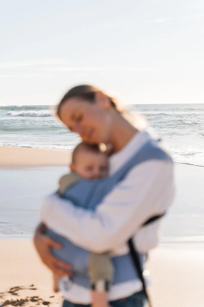 Mother carrying her baby in a sling on a Lagos beach at golden hour
