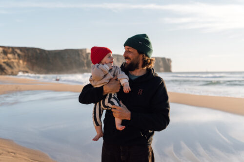 Father holding his smiling baby on a Sagres beach with dramatic cliffs at golden hour
