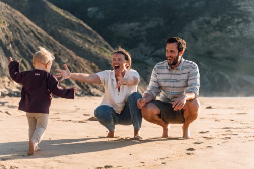 Toddler running into a parent's open arms on the beach during a family photoshoot in the Algarve