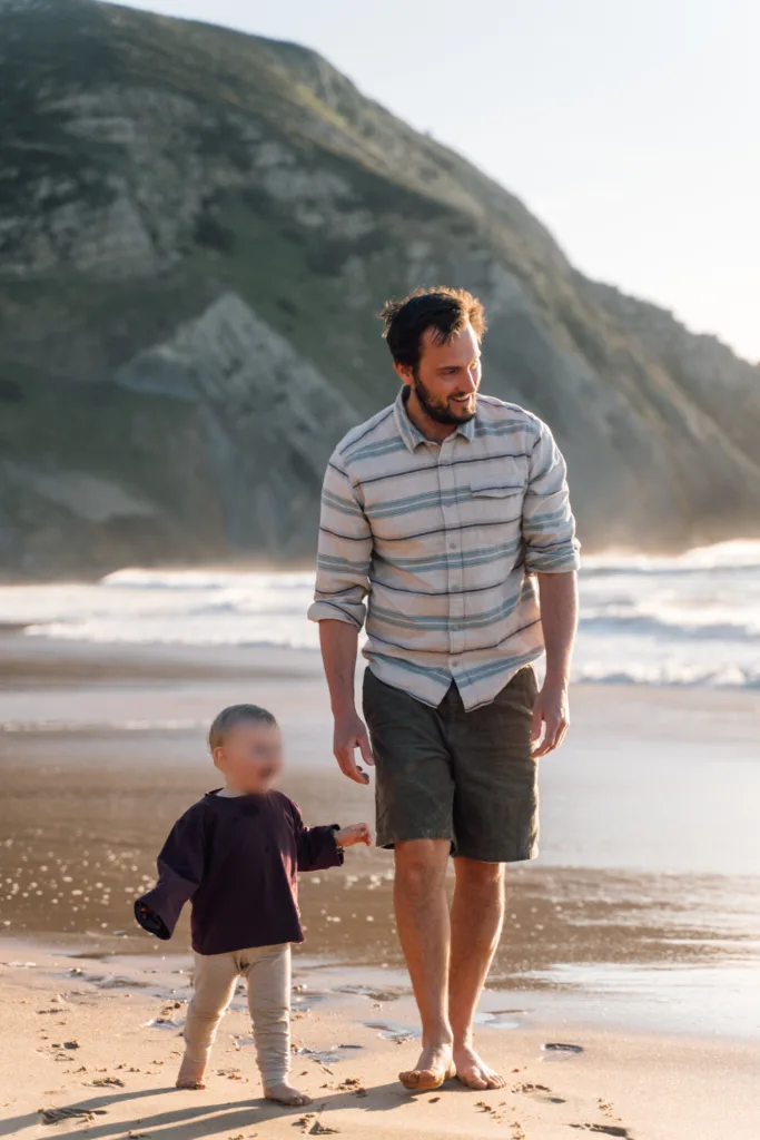 Father and toddler walking hand in hand on a Sagres beach below the cliffs