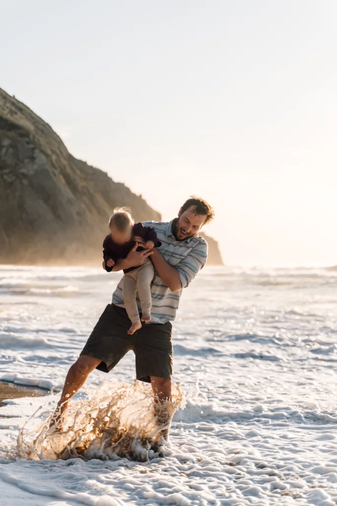 Father playfully holding his child while splashing through the waves on a Sagres beach