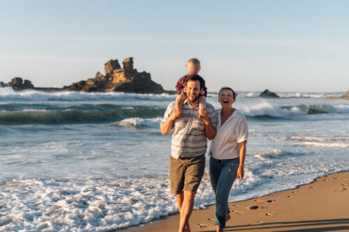 Happy family of three walking through the surf at sunset during an Algarve family photoshoot