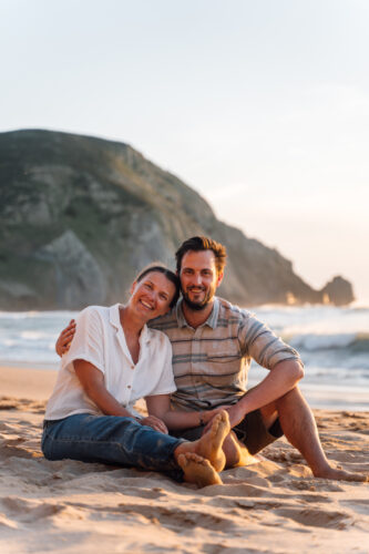 Smiling couple sitting on an Algarve beach at golden hour during a family photoshoot